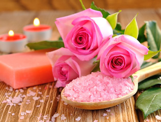 Sea salt, rose, soap and a burning candle on a brown table