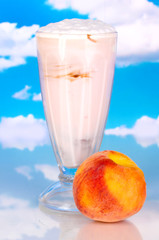 Delicious milk shake with peach on sky background