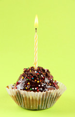 tasty birthday cupcake with candle, on green background