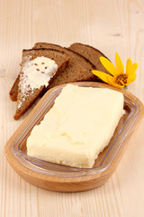 Butter on wooden holder and bread on wooden table close-up