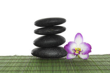 Fototapeta na wymiar Black massage stones stacked with orchid on green mat