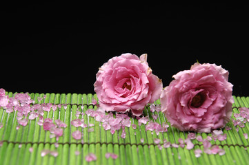 Two rose with pile of spa salt on green bamboo mat