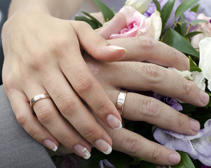 Руки молодоженов с обручальными кольцами на букете цветов