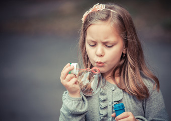 Portrait of funny lovely little girl blowing soap bubble