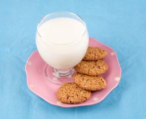 glass of milk and whole grain cookies in a ping plate on blue