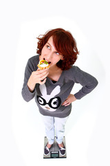 Smiling girl standing on the scales and eating cake isolated on