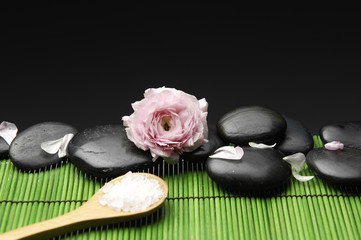 Salt in wooden spoon with pink ranunculus flower with pebble