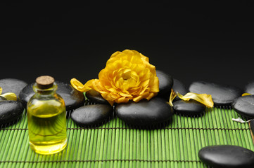 massage oil bottle and orange ranunculus with stones on mat