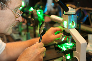 Scientist with glass, loupe configure laser of microparticles