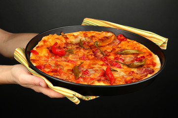 hands holding pepperoni pizza in pan on grey background