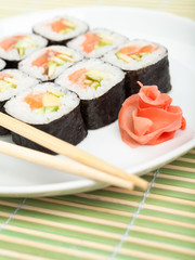 Sushi rolls on the plate with wood white chopsticks on green mat