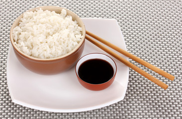 Bowl of rice and chopsticks on plate on grey mat