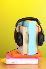 Headphones on books on wooden table on green background