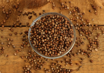Heap coriander seeds in bowl on wooden background close-up