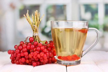 tea with red viburnum on table on bright background