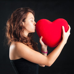 Portrait of attractive curly woman kissing red heart