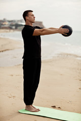 Fototapeta na wymiar muscular man does body exercises with a ball near the ocean