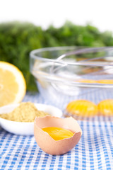 Broken eggs in bowl with lemon and mustard