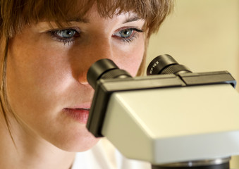 Junge Wissenschaftlerin guckt durch ein Mikroskop