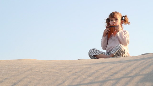little girl play panpipe in desert