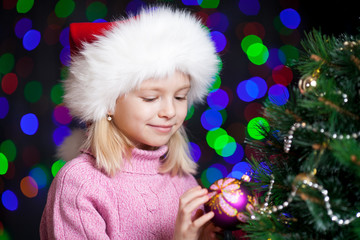 pretty preschool girl decorating Christmas tree over bright fest