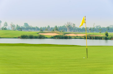 Obraz premium golf ball on green near hole with yellow flag