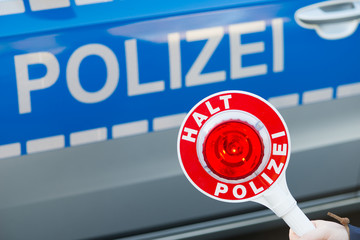 Polizist hält Polizeikelle vor Polizeiauto