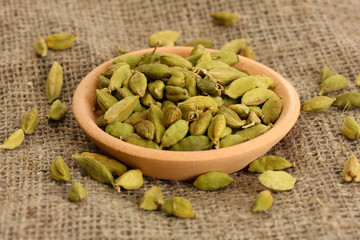Green cardamon in clay bowl on canvas background close-up