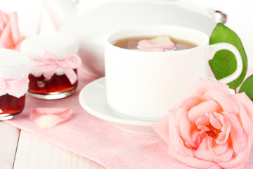 teapot and cup of tea with roses and jam on white wooden table