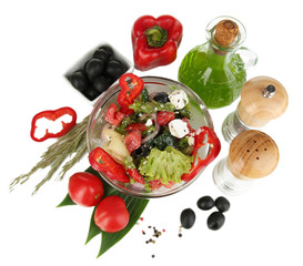Fresh greek salad in glass bowl surrounded by ingredients for