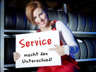 Female car mechanic presents white message board in a tire stock