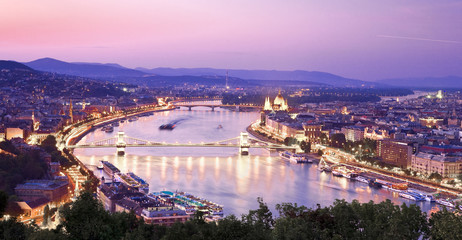 View of Budapest with Danube. Beautiful crimson sunset over Budapest. View of the evening city, houses, the parliament building. The sky is reflected in the river. Mountains in the background.