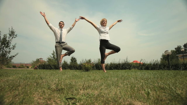 Wide shot of Caucasian male and female office workers standing barefoot on lawn, practicing yoga during break time. Suitable for corporate lifestyle, mindfulness and wellness content