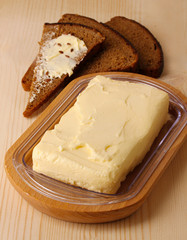 Butter on wooden holder and bread on wooden table close-up