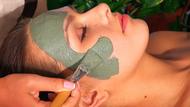 Woman with clay facial mask in beauty spa.
