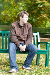 Obraz premium young man in the autumn park sitting on bench