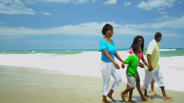 African American parents walking and chilling with children holding hands on beach 
