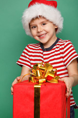 Funny child in Santa red hat holding Christmas gift in hand.