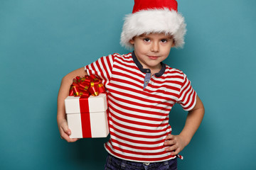 Funny child in Santa red hat holding Christmas gift in hand.