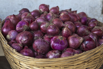 A basket full with red/ purple unions with a white wall in the b