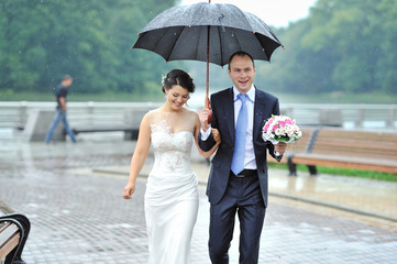 Young happy bride and groom walking by the rain