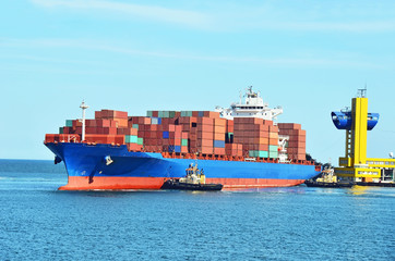 Tugboat assisting container cargo ship to harbor quayside