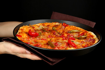 hands holding pepperoni pizza in pan isolated on black