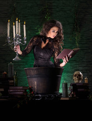 A young brunette witch in a dark dress making a mystical posion