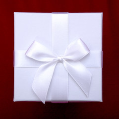 beautiful white gift box with ribbon on top of red sofa