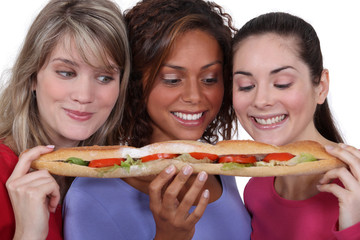 Three female friends sharing long sandwich