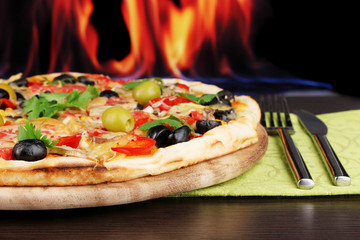 Delicious pizza close-up on wooden table on fire background