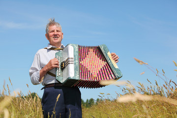 Grandfather in shirt play on accordion, sing in field