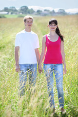 young couple hold hands in field near village