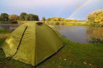 Green tent pitched on the bank of a lake.